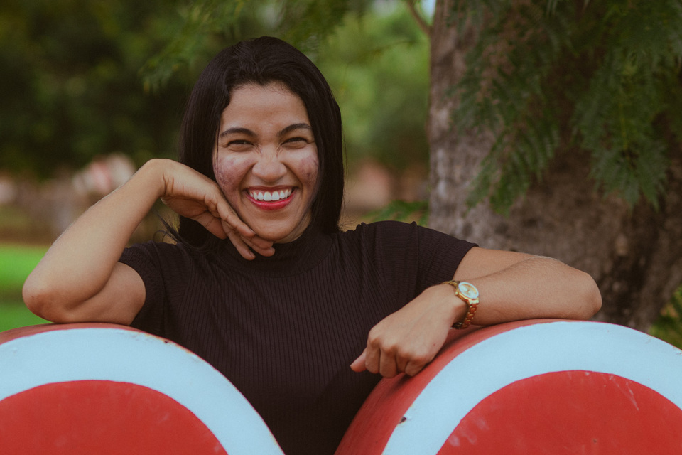mulher de pele parda, blusa preta e com pose sorrindo para foto